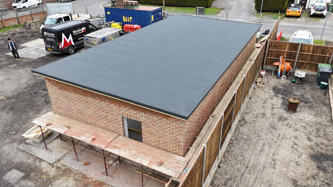 Flat roof installation on a brick building under construction, showcasing modern roofing systems in a construction site setting.