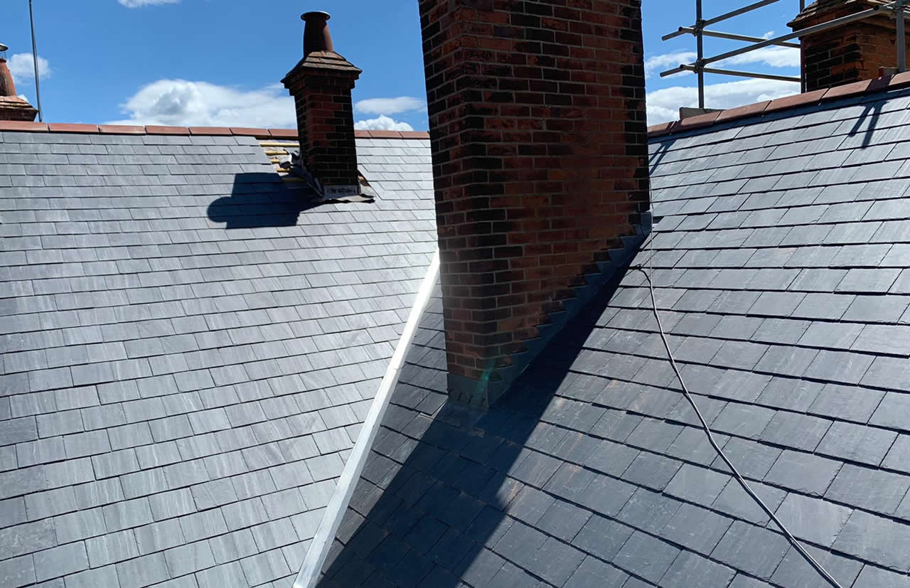 Slate roof with chimney and lead flashing on a listed building, showcasing roofing details relevant to heritage architecture.