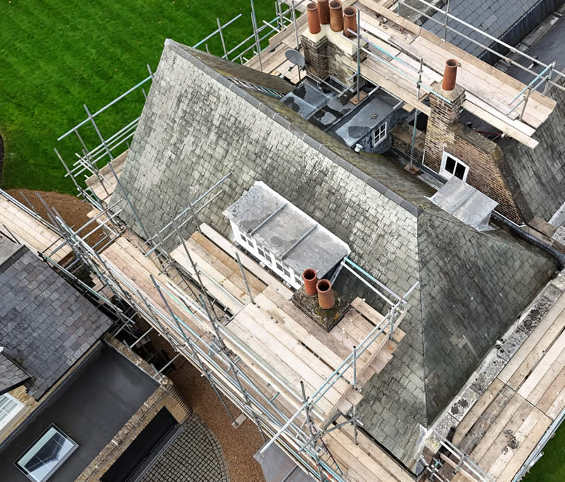 Aerial view of a traditional slate roof with chimney stacks, surrounded by scaffolding, highlighting ongoing roofing work for heritage and conservation properties.
