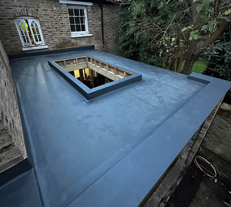 Flat roof with modern three-layer felt system, featuring a skylight opening, surrounded by brick walls and greenery, illustrating durability and discreet appearance for heritage properties.