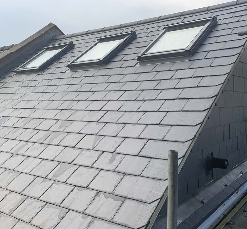 Slate roof with three modern Velux windows, showcasing precise installation and minimal disruption, emphasizing energy efficiency and aesthetic integration.