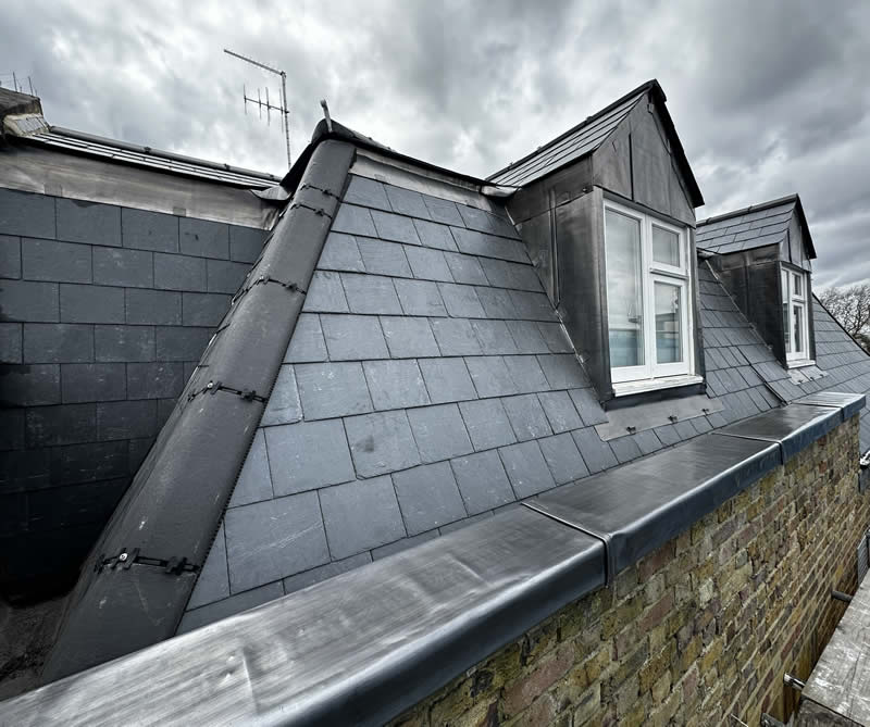 Slate roof installation with prominent gable features and chimney, showcasing quality craftsmanship and attention to heritage details in a domestic setting.