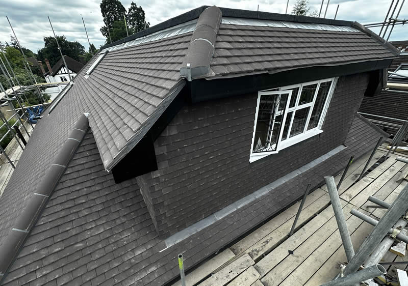 Roof of a loft conversion featuring dark shingles, a window with decorative detailing, and scaffolding, illustrating expert roofing integration for extensions and structural continuity.