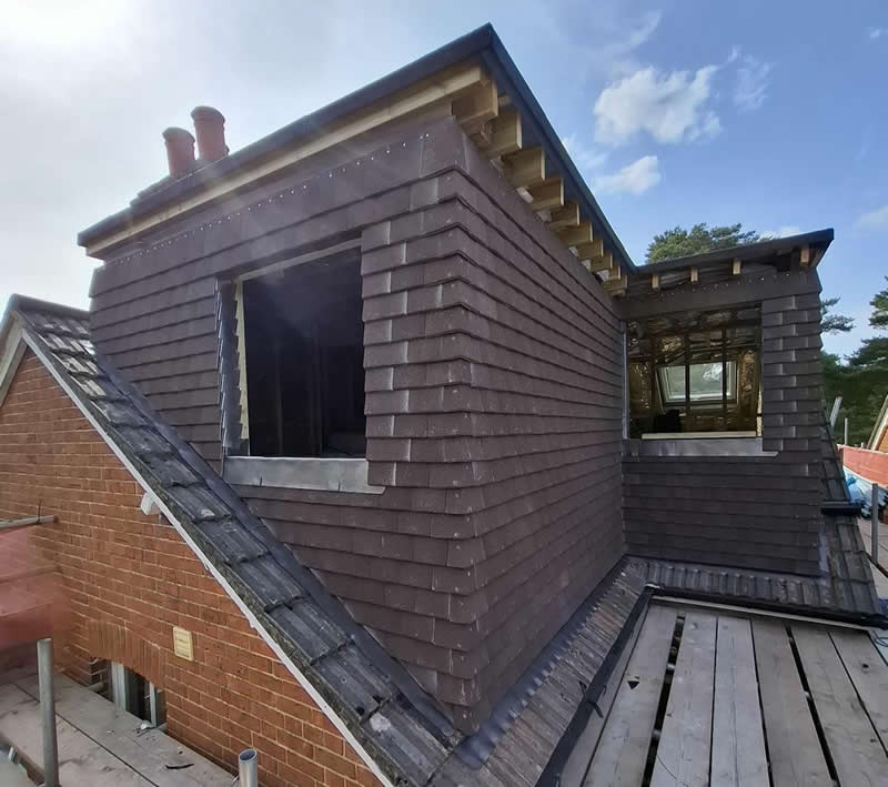 Loft extension with modern roofing featuring slate tiles and a window frame, showcasing integration with existing structure in a heritage property context.