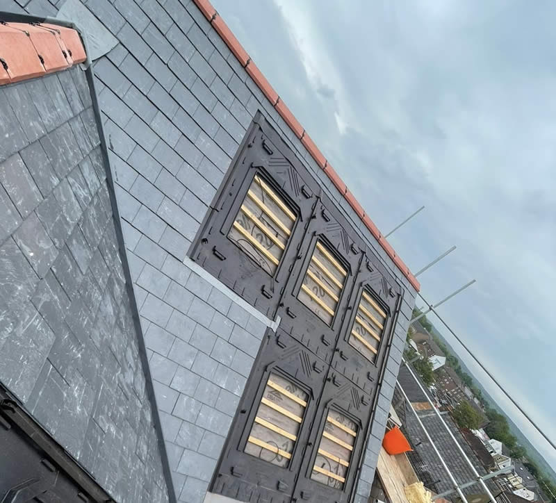 Roof featuring slate tiles and decorative black leadwork, showcasing windows under construction, with scaffolding in the background, representing professional roofing services by Precision Leadwork & Roofing Ltd.