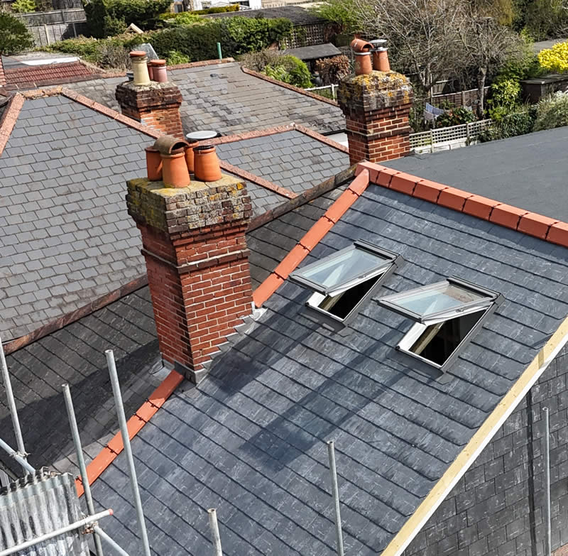 Chimney stacks with terracotta pots atop a slate roof, showcasing heritage architecture and structural integrity, emphasizing restoration and repair services by Precision Leadwork & Roofing Ltd.